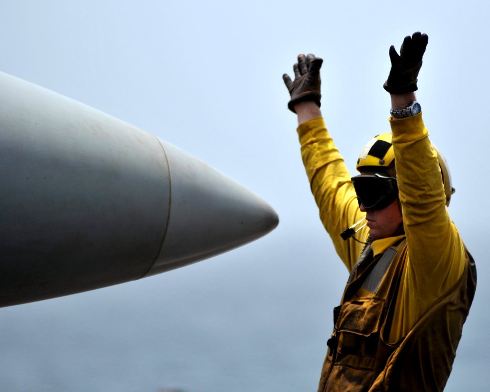 US Navy 080814-N-7981E-096 Aviation Boatswain's Mate (Handling) Airman Sean Bibby directs an F-A-18E Super Hornet