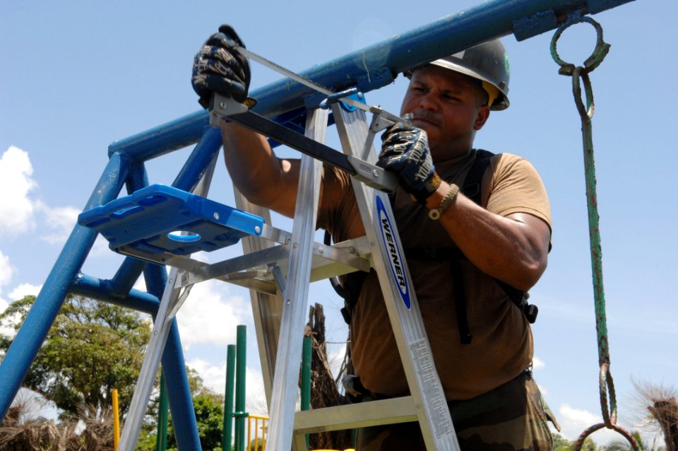 US Navy 080816-N-7544A-133 Equipment Operator 2nd Class Carlos Guzman, embarked aboard the amphibious assault ship USS Kearsarge (LHD 3), saws a piece of metal to remove a broken swing before new playground equipment can be ins
