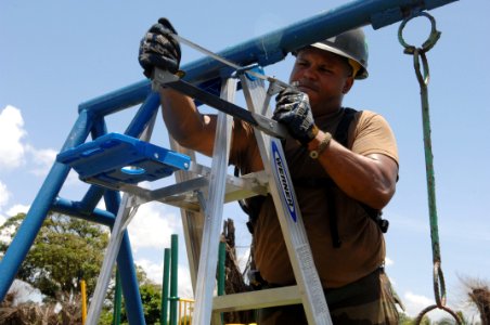 US Navy 080816-N-7544A-133 Equipment Operator 2nd Class Carlos Guzman, embarked aboard the amphibious assault ship USS Kearsarge (LHD 3), saws a piece of metal to remove a broken swing before new playground equipment can be ins photo