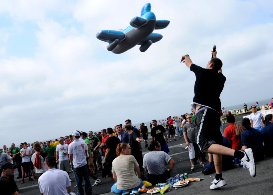 US Navy 080822-N-9898L-463 Yeoman 3rd Class Bryan Patino, from Imperial Beach, Calif., tosses an airplane-shaped pool toy into the audience during a break in a karaoke session during a steel beach picnic on the flight deck of t