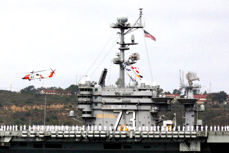 US Navy 080821-N-3446M-660 A U.S. Coast Guard helicopter escorts the aircraft carrier USS George Washington (CVN 73) as she departs Naval Air Station North Island