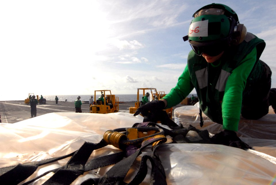 US Navy 080823-N-7730P-054 Store Keeper 3rd Class Chelsea Demoss unbuckles the cargo netting around a pallet delivered to the flight deck of the Nimitz-class aircraft carrier USS Ronald Reagan (CVN 76)