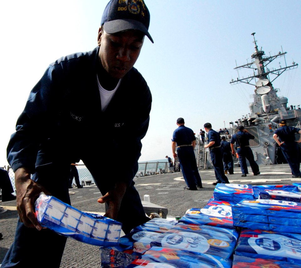 US Navy 080824-N-4044H-106 Boatswain's Mate Seaman Recruit Eddius Hucks stacks humanitarian aid supplies aboard the guided-missile destroyer USS McFaul (DDG 74), which will be put on pallets and distributed to the people of Geo