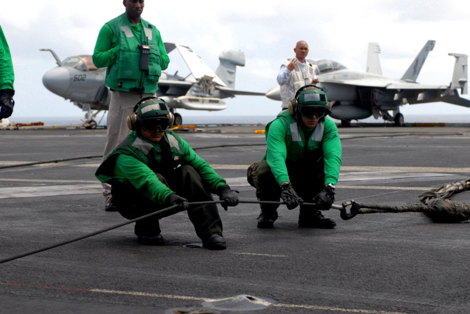 US Navy 080827-N-3610L-003 Two flight deck personnel aboard the Nimitz-class aircraft carrier USS Ronald Reagan (CVN 76) stretch an arresting gear cable