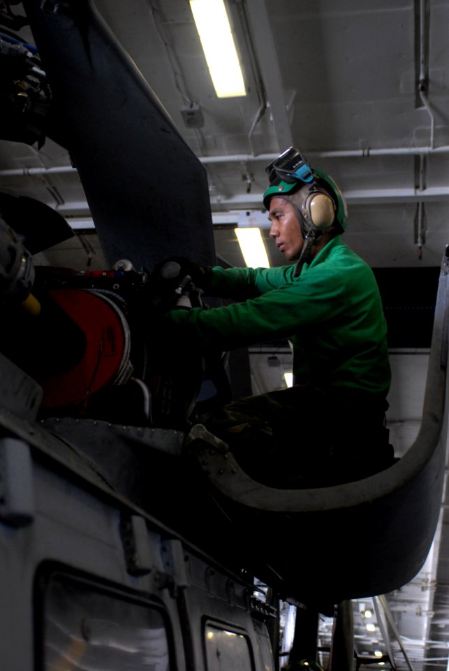 US Navy 080829-N-3610L-162 Aviation Machinist's Mate 1st Class Joselito Camiling perches himself on a HH-60H Sea Hawk to perform routine maintenance in hangar bay 1 aboard USS Ronald Reagan (CVN 76)