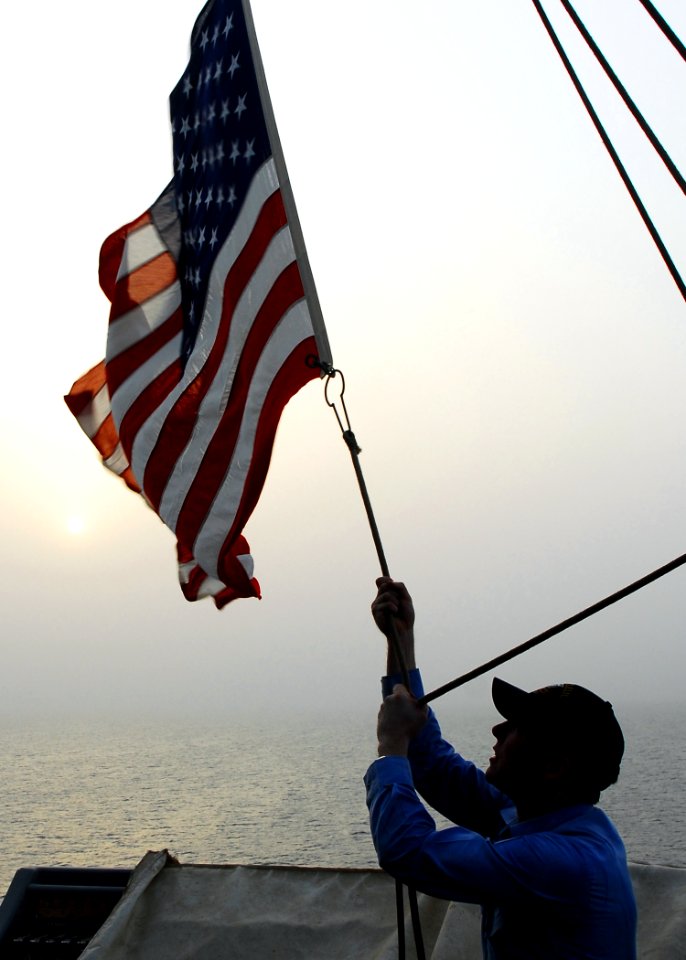 US Navy 080911-N-2183K-036 Mass Communication Specialist 2nd Class Scott A. Webb lowers a flag to half-mast at sunset aboard the amphibious assault ship USS Peleliu (LHA 5) to honor those lost during the attacks on Sept. 11, 20