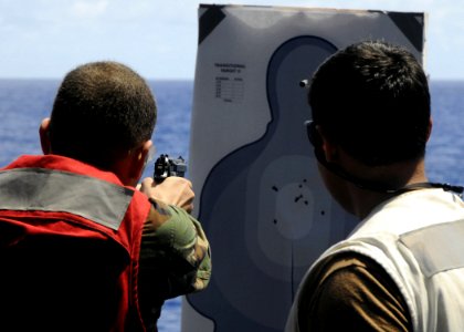 US Navy 080914-N-2638R-001 Master-at-Arms 2nd Class Isidoro Claudio shoots a 9mm pistol as Aviation Ordnanceman Airman Jorge Vega watches