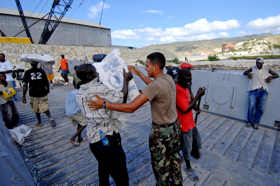 US Navy 080923-N-9620B-004 Boatswain's Mate 3rd Class Christian Farfan, embarked aboard the amphibious assault ship USS Kearsarge (LHD 3), helps a Haitian relief worker unload food and water to aid those affected by recent hurr