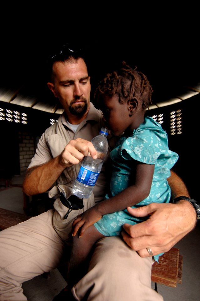 US Navy 080924-N-9620B-009 Naval Criminal Investigative Service Special Agent Jeremy Gouthier, assigned to the amphibious assault ship USS Kearsarge (LHD 3), gives a Haitian girl a drink of water during a medical assessment