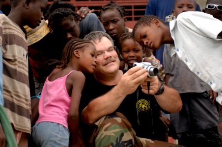 US Navy 080924-N-9620B-015 Cmdr. Dale Bates, of the U.S. Public Health Service, entertains a Haitian children with photos after conducting a health assessment in their village to determine future medical aid