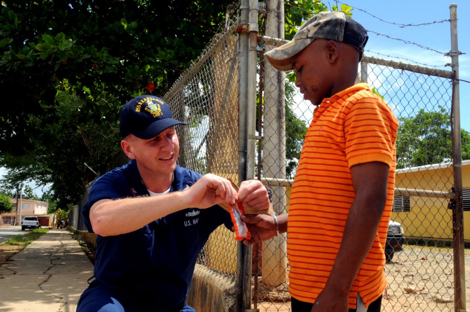 US Navy 081004-N-9774H-064 Information Systems Technician 1st Class Randy Lambert, assigned to the amphibious assault ship USS Kearsarge (LHA 3) gives candy from his meals ready to eat to a Dominican Republic child