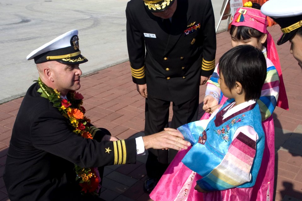 US Navy 081008-N-9123L-004 Cmdr. John S. Banigan, commanding officer of the guided-missile destroyer USS John S. McCain (DDG 56), gives a Korean child a ship's coin after receiving a traditional flower wreath presented to welco