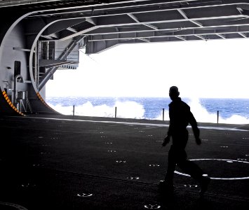 US Navy 081010-N-9610C-006 A Sailor walks through the hangar bay as waves crash against the hull of the Nimitz-class aircraft carrier USS John C. Stennis (CVN 74)