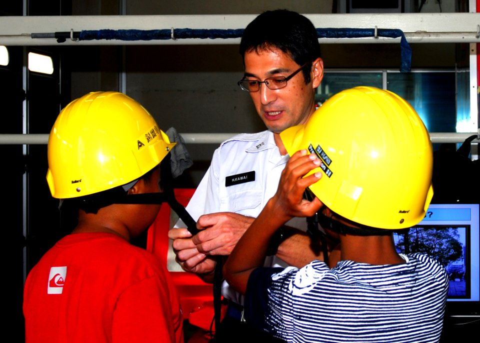 US Navy 081007-N-0483B-003 Hiroaki Kawai, a member of Yokosuka's Commander Naval Forces Japan (CNFJ) Regional Fire Department, assists students from The Sullivans Elementary School as they don safety helmets