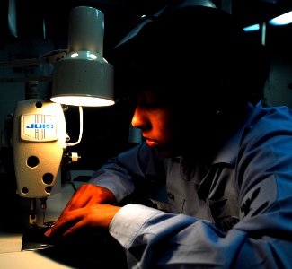US Navy 081011-N-9610C-034 Aviation Boatswain's Mate (Handling) 3rd Class Dayanis Savon sews a uniform patch onto coveralls