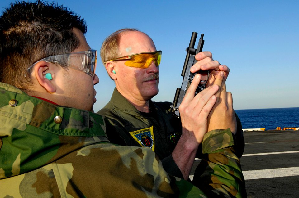 US Navy 081012-N-4954I-007 Gunner's Mate Seaman Joel Ramirez, left, from Glendale, Ariz. hands a 9mm pistol to Carrier Strike Group (CSG) 3 commander Rear Adm. Mark Vance, during a small-arms certification