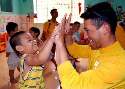 US Navy 100812-N-8539M-139 Operations Specialist 3rd Class Angel Ramirez practices high-fives with a child at a Da Nang primary school