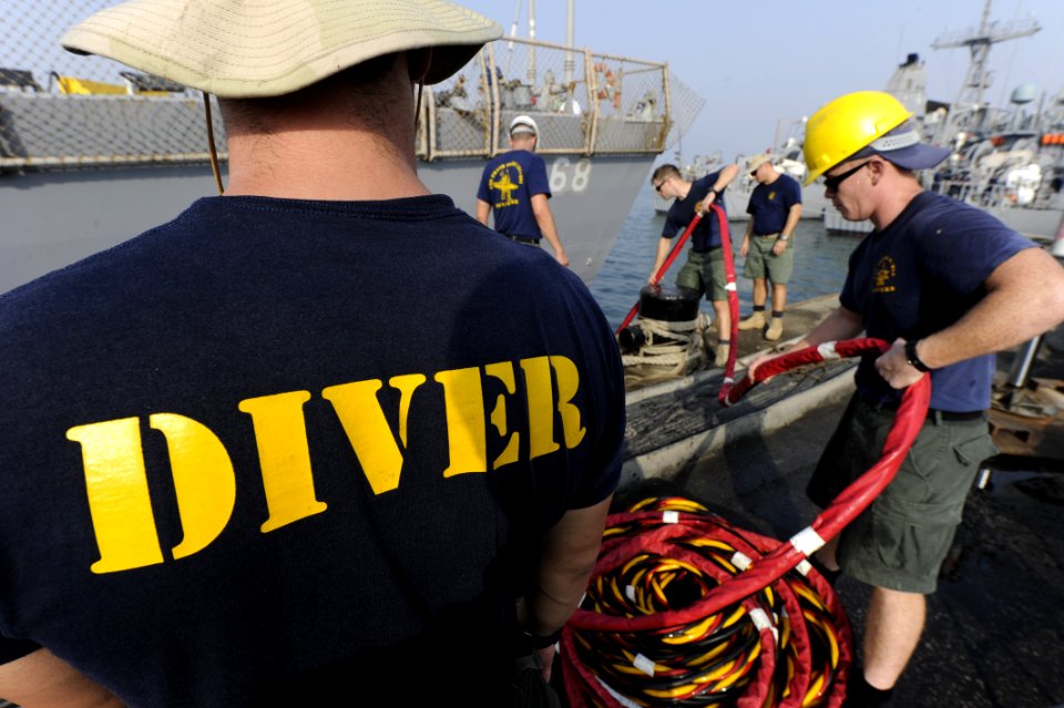 US Navy 100616-N-4776G-753 Navy divers loop excess air hose in a coil as they assist a diver out of the water