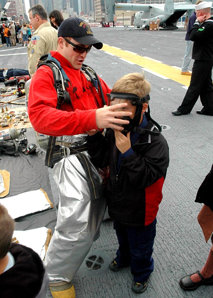 US Navy 081013-N-6439C-036 Aviation Boatswain's Mate (Handling) 3rd Class Paul Bria puts a firefighting mask on a child during a tour of the amphibious assault ship USS Nassau (LHA 4)