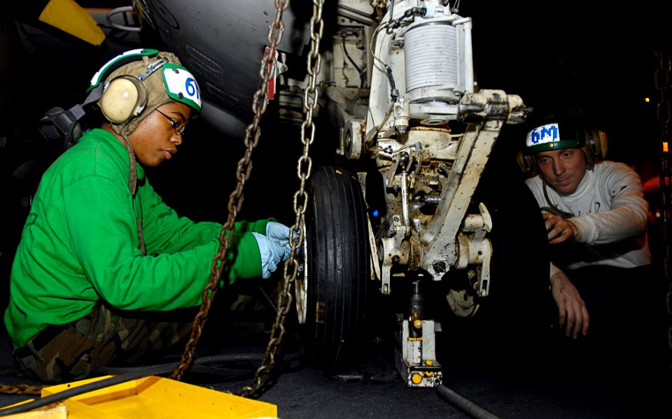 US Navy 081020-N-4954I-003 Aviation Structural Mechanic 3rd Class Amber Scott and Aviation Structural Mechanic 3rd Class Mike Vaneerde tighten screws on the landing gear of an E-2C Hawkeye