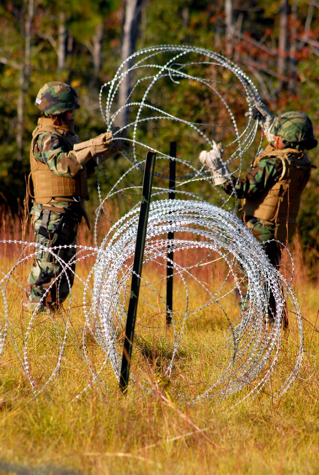 US Navy 081104-N-7367K-009 Gunner's Mate 2nd Class Amanda Hung, left, and Gunner's Mate 2nd Class Ava Dean, both assigned to Naval Mobile Construction Battalion (NMCB) 1, set up concertina wire around the ammunition supply poin