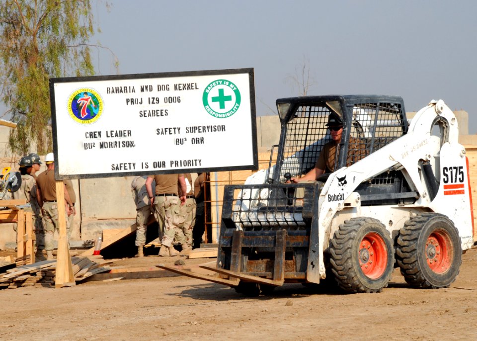 US Navy 081106-N-1120L-072 A Seabee assigned to Naval Mobile Construction Battalion (NMCB) 7 drives a Bobcat past the construction site of a temporary military working dog kennel facility
