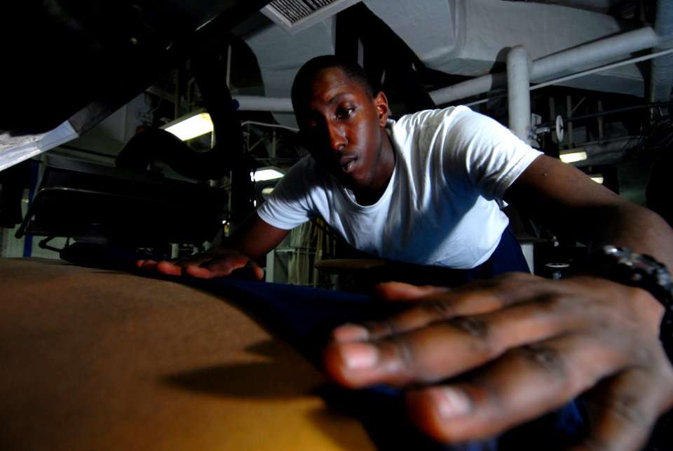 US Navy 081120-N-9950J-055 Mass Communication Specialist Seaman Apprentice Taurean Alexander, from Fresno, Calif., creases a pair of coveralls while working as a laundry service assistant in the laundry room of the forward-depl