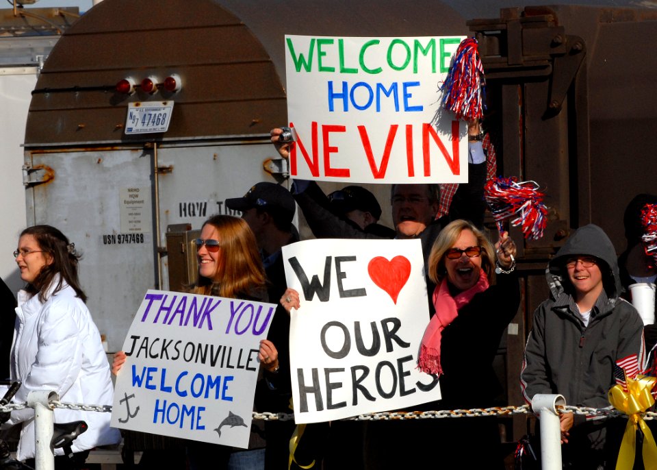 US Navy 081124-N-7668G-033 Family members of the crew of the Los Angeles-class attack submarine USS Jacksonville (SSN 699) hold up signs while observing the submarine's return from a six-month deployment