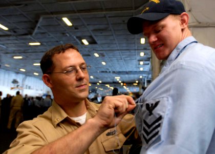 US Navy 081123-N-2456S-052 Chief Machinist's Mate William Garnett sews the first class petty officer crow onto newly frocked Machinist's Mate 1st Class Nicholas Dover's uniform