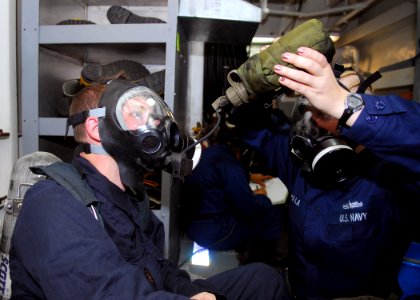 US Navy 081203-N-2013O-017 Ship's Serviceman 3rd Class Amanda Rampulla, from Wapakoneta, Ohio, helps Culinary Specialist 2nd Class Vaughn Green, from Mesa, Ariz., drink water through a MCU-2P gas mask