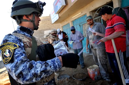US Navy 081206-N-1810F-259 An Iraqi National Policeman hands out leaflets to Iraqi civilians during a walking patrol through the Rashid community in Bahgdad photo