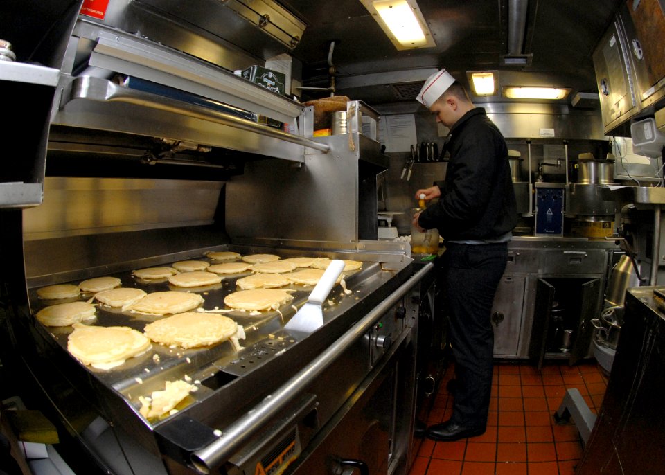 US Navy 081210-N-7668G-018 Culinary Specialist Seaman Apprentice Henry Kennedy, from Opelousas, La., prepares eggs as pancakes cook on the grill aboard the Los Angeles-class attack submarine USS Albany (SSN 753)