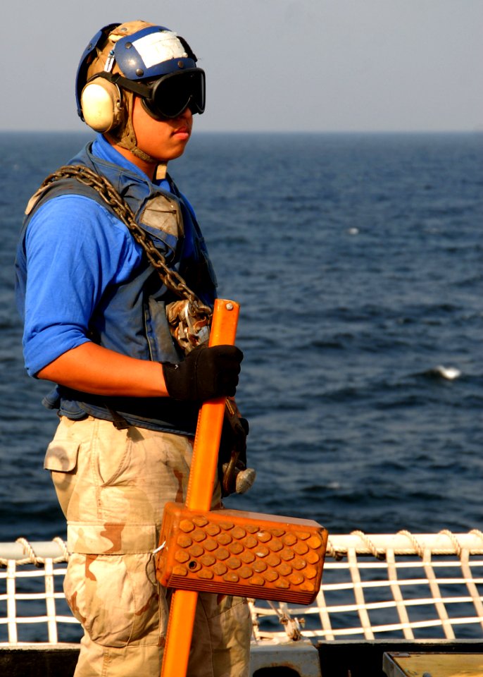 US Navy 081215-N-9134V-003 Seaman Daniel Nguyen, from Van Nuys, Calif., stands ready to chock and chain an incoming helicopter aboard the amphibious dock landing ship USS Carter Hall (LSD 50)