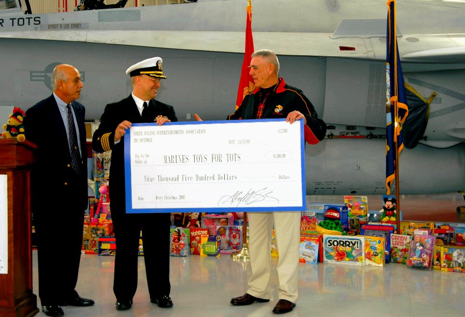 US Navy 081216-N-5617R-047 Capt. Michael Kelly, commanding officer of Fleet Readiness Center Southwest, presents toys and a check to retired Gunnery Sgt. R. Lee Ermey to benefit the Marine Corps Reserve Toys for Tots program