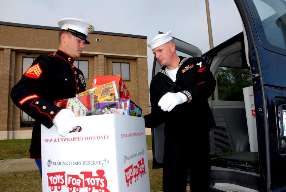 US Navy 081218-1057H-N-303 Marine Corps Sergeant Jeffrey Kellum hands a box of donated toys to Hospital Corpsman 2nd Class Christopher Long