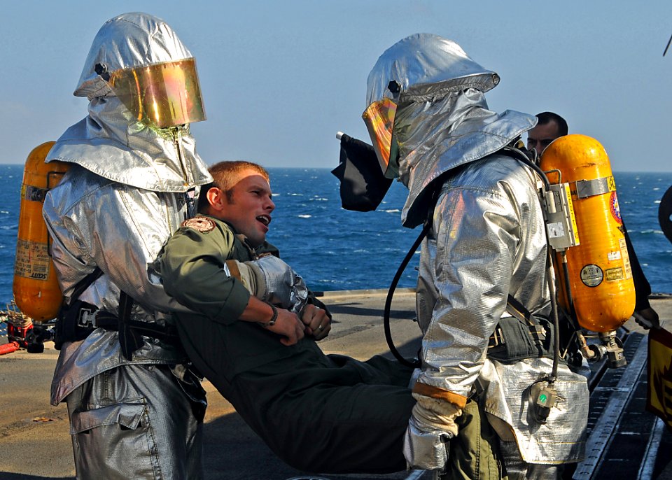 US Navy 081231-N-1082Z-044 Boatswain's Mate 3rd Class Christophor Villar and Seaman Kendall A. Reep carry Aircrewman 2nd Class William S. Stevens o safety during a flight deck fire drill