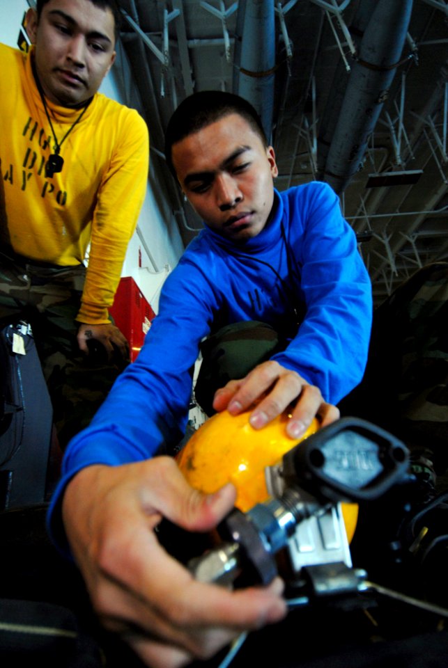 US Navy 090116-N-3946H-032 Aviation Boatswain's Mate 3rd Class Michael Melgar supervises Aviation Boatswain's Mate Airman Apprentice Enrico Rabina through the process of removing a self-contained breathing apparatus (SCBA) bott