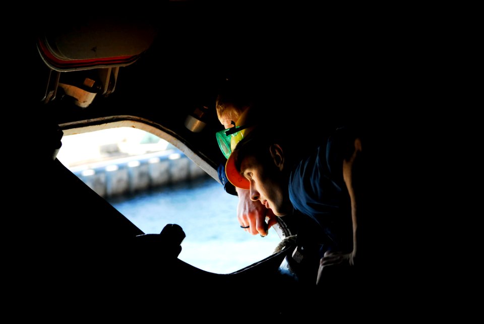 US Navy 090116-N-9610C-003 Boatswain's Mate 3rd Class Lance Reynolds, from Powhatan, Va., peers out a hatch to check the position of the aircraft carrier USS John C. Stennis (CVN 74)