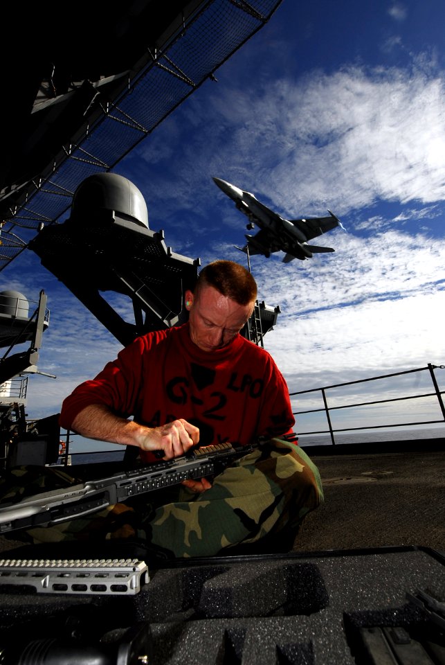 US Navy 090119-N-9610C-008 Gunner's Mate 1st Class Jory Judd cleans an M-14 sniper rifle on the fantail as an F-A-18C Hornet from the