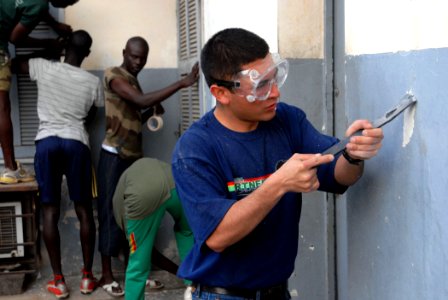 US Navy 090205-N-1688B-056 Gunner's Mate 3rd Class Santos Oyoque, assigned to the amphibious transport dock ship USS Nashville (LPD 13), scrapes cracked paint before re-painting the walls of the Centoe Mecico Social clinic