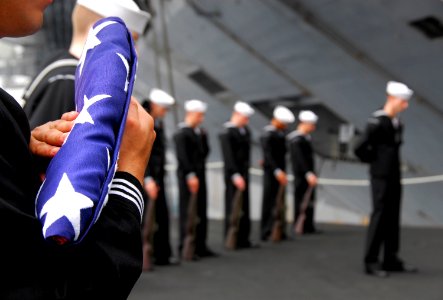 US Navy 090216-N-6597H-104 Religious Program Specialist Pablo Monroy, from Pasco, Wash., holds an American flag during a burial-at-sea service on aircraft elevator four aboard the Nimitz-class aircraft carrier USS John C. Stenn
