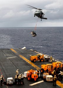 US Navy 090301-N-9950J-012 Sailors and Marines move pallets as an MH-60S Sea Hawk helicopter drops off supplies aboard USS Essex (LHD 2)