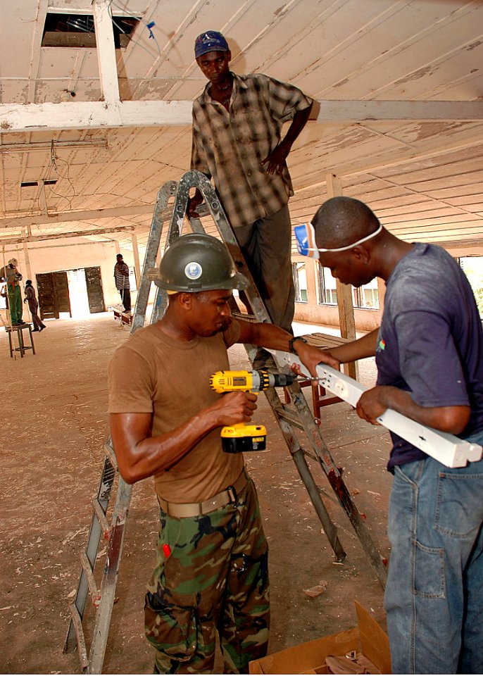 US Navy 090302-N-1655H-449 Construction Electrician 2nd Class Darius Michael, assigned to Naval Mobile Construction Battalion (NMCB) 11, works with Ghanaian Navy sailors to install a light fixture during a refurbishment project