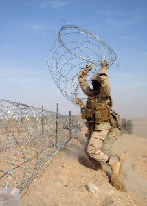 US Navy 090320-N-8574M-034 A Seabee assigned to Naval Mobile Construction Battalion (NMCB) 5 lifts concertina wire to complete a section of a triple-strand protective barrier