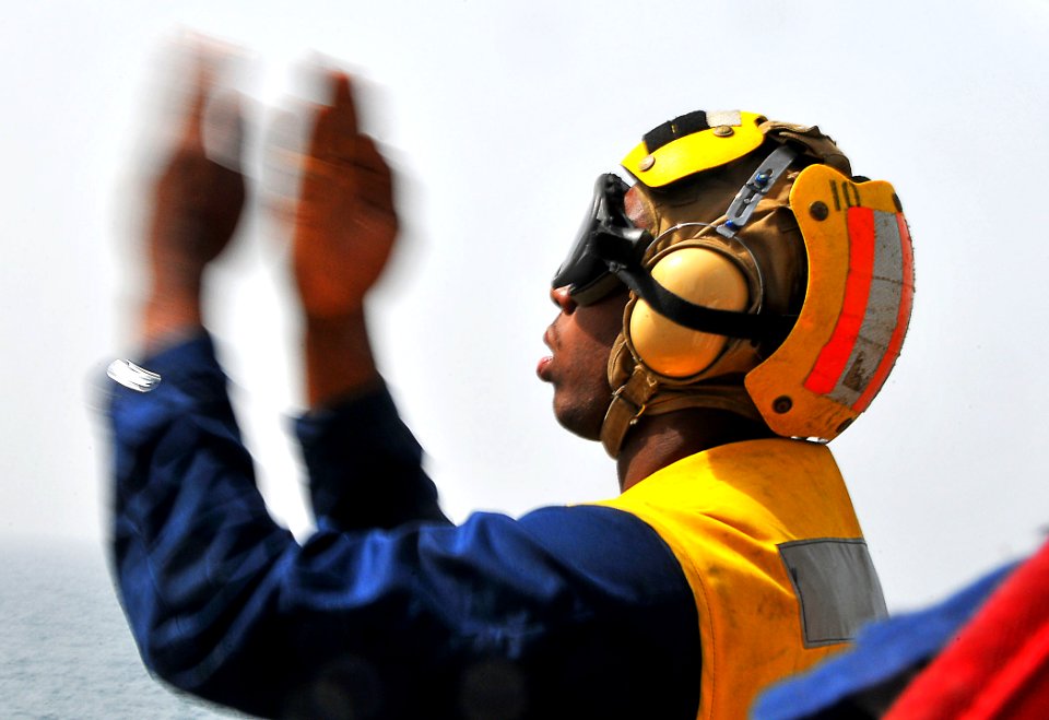 US Navy 090324-N-4774B-047 Boatswain's Mate Seaman Dana Arnett gives flight signals to a helicopter delivering supplies aboard the guided-missile cruiser USS Lake Champlain (CG 57)