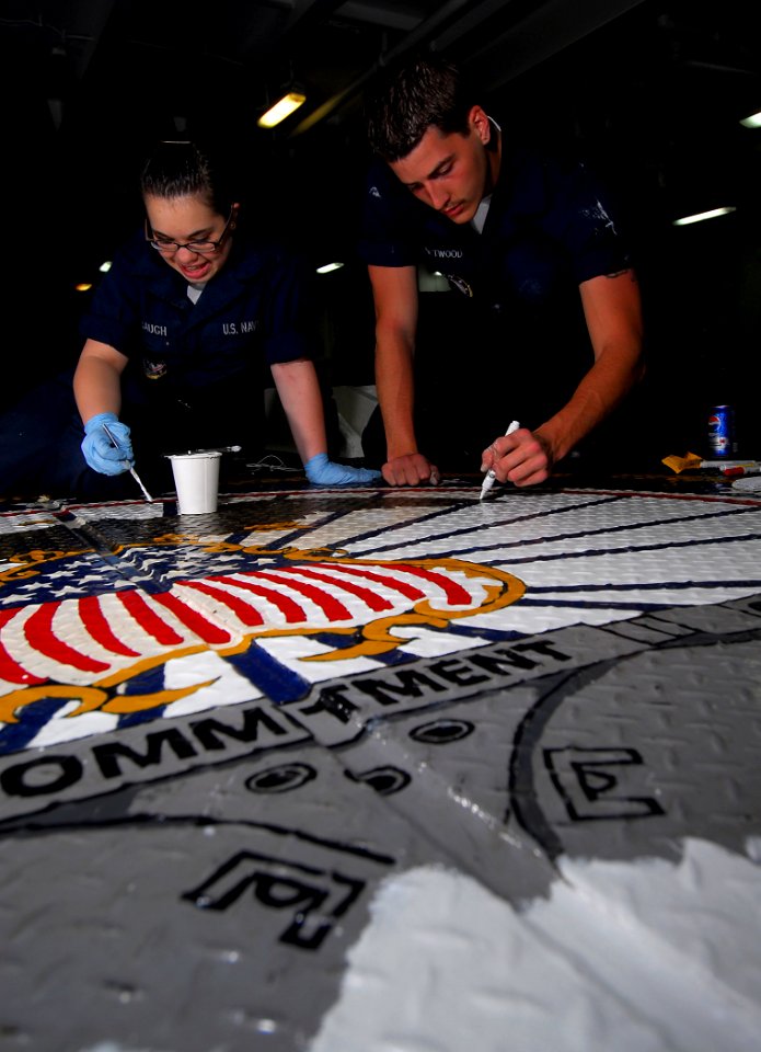 US Navy 090326-N-6597H-012 Seaman Courtney Alumbaugh, left, from Great Lakes, Ill., and Boatswain's Mate Seaman Alex Chetwood, from Cedar Grove, Ind., repaint the command seal on the deck in the forecastle