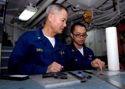 US Navy 090422-N-9520G-006 Cmdr. Chin Van Dang, a native of Vietnam and command chaplain aboard the amphibious assault ship USS Essex (LHD 2), goes over ideas for candle holders for the ship's chapel with Aviation Structural Me