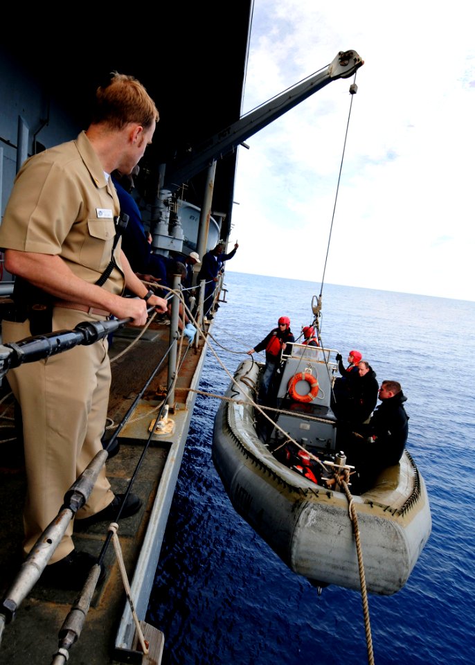 US Navy 090502-N-4044H-016 Cargo Mate David Dezutter, a Military Sealift Command safety observer, watches as a rigid hull inflatable boat is lifted out of the water after a man overboard drill