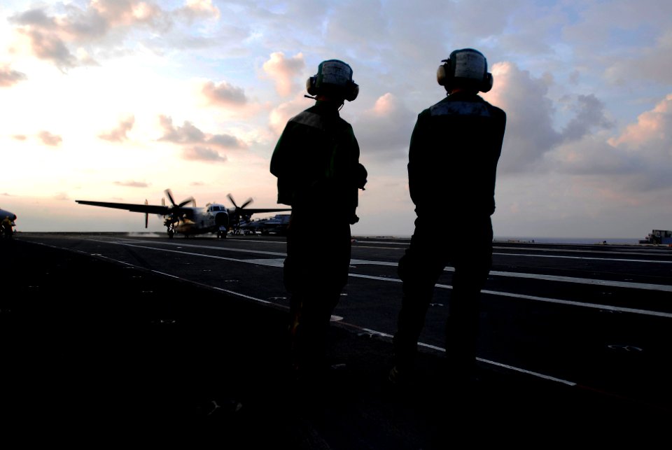 US Navy 090504-N-6538W-177 Aviation Boatswain's Mate Airman Andrew Sallee, left, from Parma, Idaho, and Aviation Boatswain's Mate 3rd Class John Symonds, from Houston, Texas, watch as a C-2A Greyhound lands aboard the aircraft