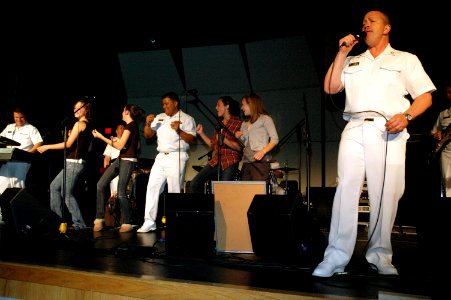 US Navy 090527-N-7975R-006 Musician 1st Class Ira Ostrowski sings lead vocals with the Naval Academy Band, the Electric Brigade, as Chief Musician Frank Dominguez dances with students during a performance at Irondequoit High